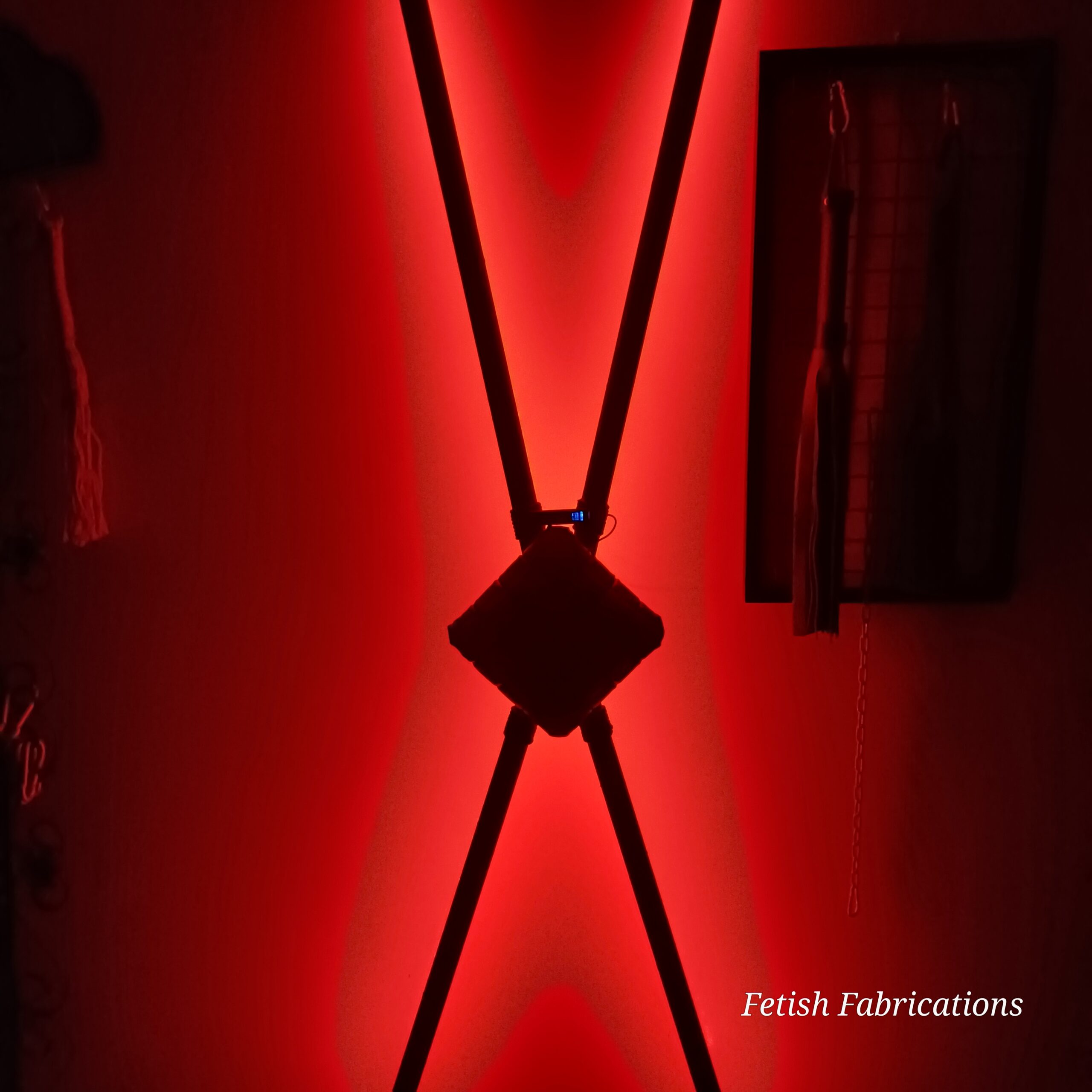 Fetish Fabrications St Andrew's Cross under red lighting, ready for a pre-use inspection
